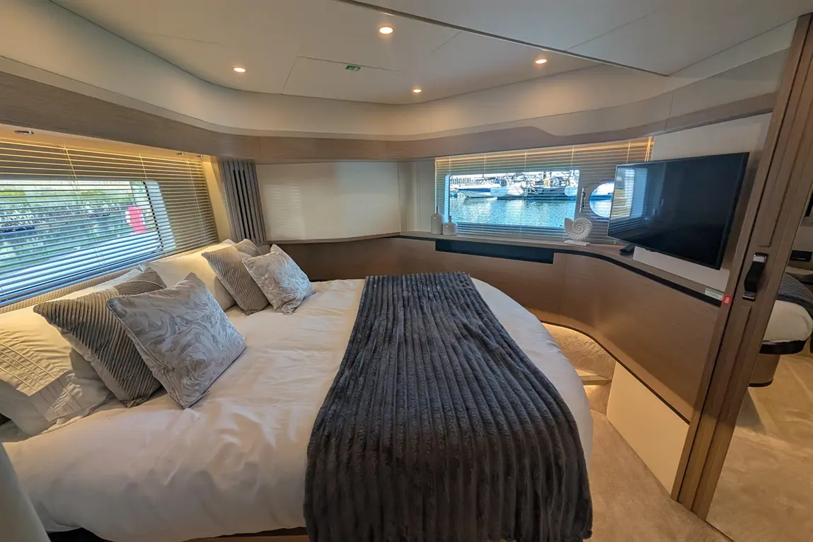 Luxury yacht bedroom with a large bed, decorative cushions, wood finishes, and a view of the marina through large windows.